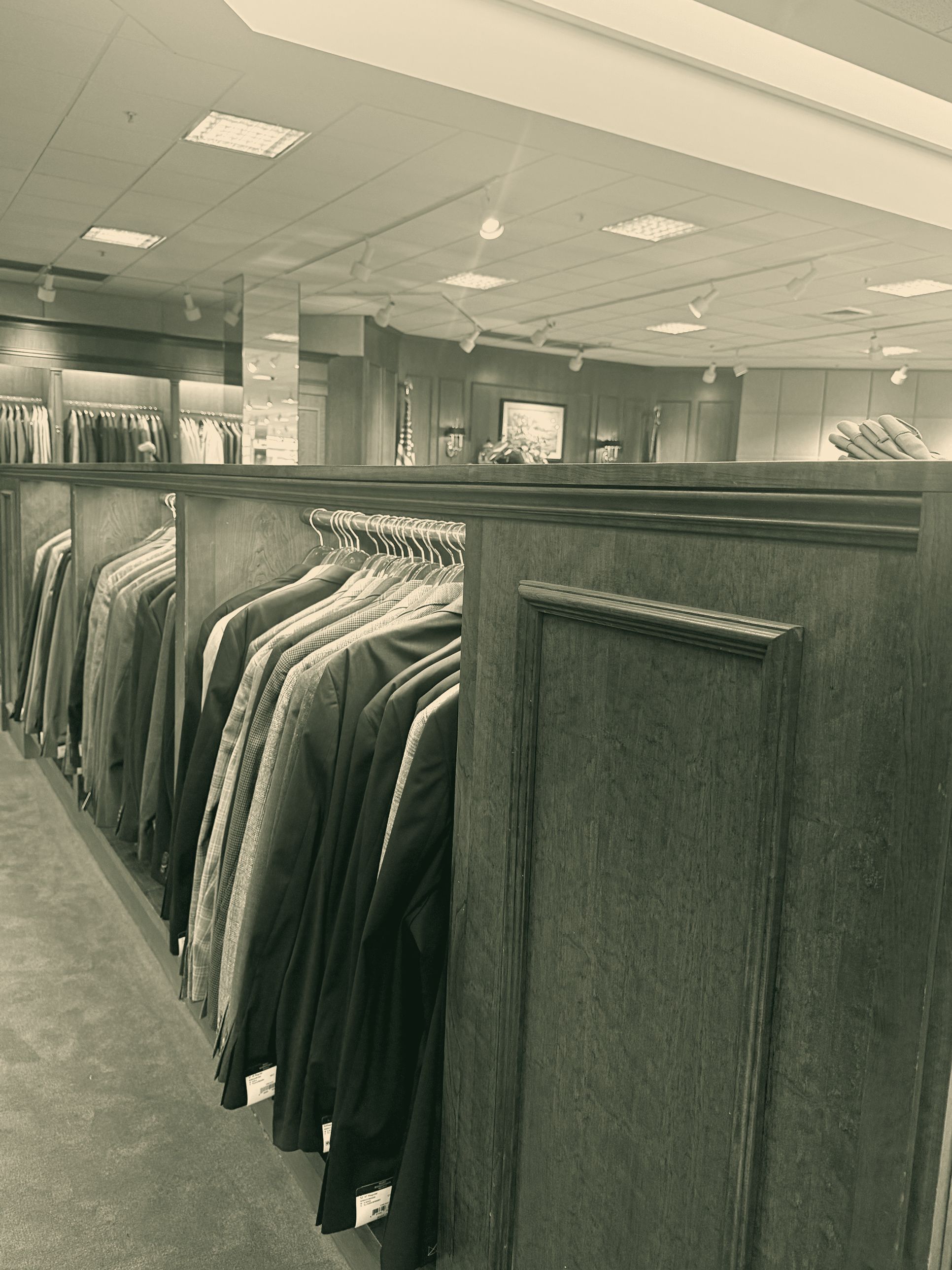 Rows of tailored jackets on a wood-paneled rack in a quiet menswear store.